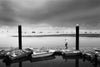 a man walks along a pontoon with dinghy boats tied up on a cloudy day with calm water