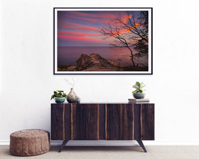 sunset over the ocean with wispy red clouds framed wall art print on the wall above a retro buffet cupboard