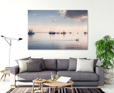a pelican swims along on calm waters with boats in the background peaceful wall art canvas in a living room with neutral sofa