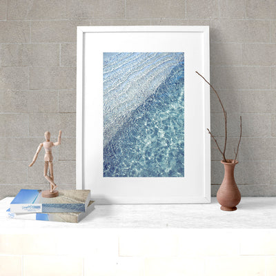 modern wall art print of blue water ocean ripples in a white frame leaning against the wall on a white desk