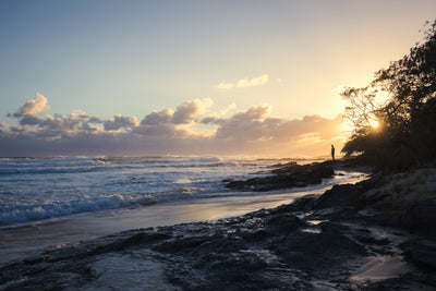 a man looks over the ocean as the sun rises through the trees on North Stradbroke island